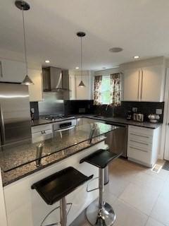 100 E 6th St Unit 2, Dracut, MA 01826 - kitchen with wall chimney range hood, dark countertops, a breakfast bar area, stainless steel appliances, and pendant lighting