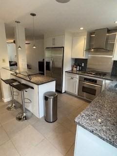 100 E 6th St Unit 2, Dracut, MA 01826 - kitchen featuring appliances with stainless steel finishes, wall chimney range hood, a kitchen bar, hanging light fixtures, and light tile patterned flooring