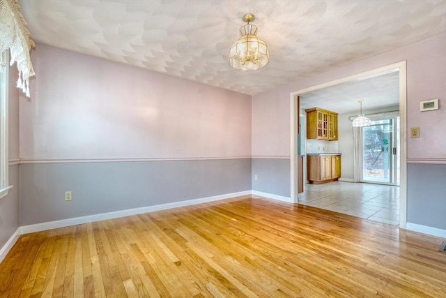 unfurnished room with light wood-style flooring, baseboards, and an inviting chandelier