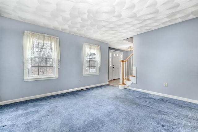 carpeted spare room featuring stairway, a textured ceiling, and baseboards