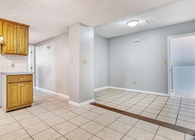 kitchen featuring tasteful backsplash, brown cabinetry, baseboards, light countertops, and light tile patterned flooring