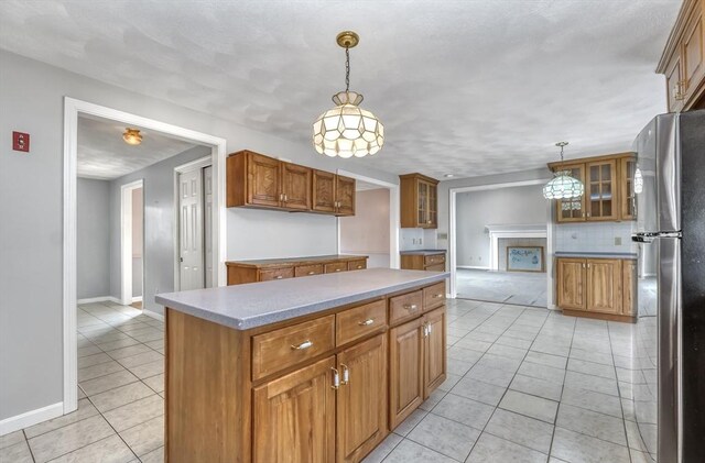 kitchen with tasteful backsplash, hanging light fixtures, brown cabinets, freestanding refrigerator, and light tile patterned flooring