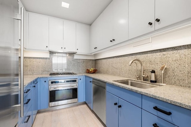 kitchen featuring sink, appliances with stainless steel finishes, backsplash, white cabinets, and blue cabinets