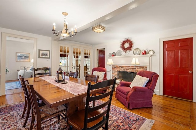 dining room with french doors, an inviting chandelier, light hardwood / wood-style flooring, and a brick fireplace