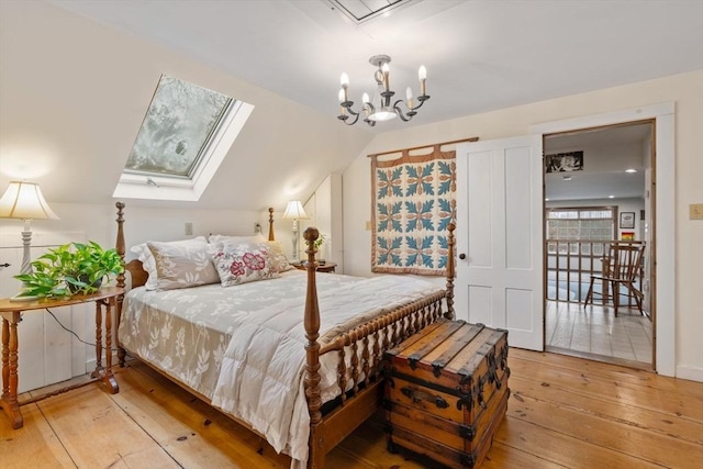 bedroom with lofted ceiling with skylight, an inviting chandelier, and light wood-type flooring