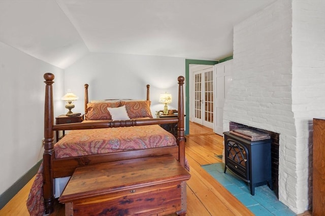 bedroom featuring a wood stove, lofted ceiling, and light wood-type flooring