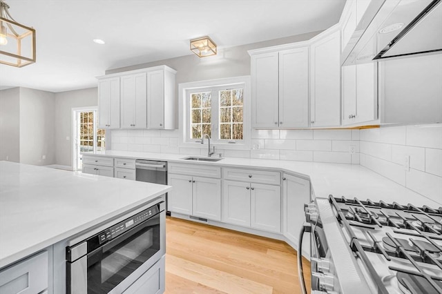 kitchen featuring tasteful backsplash, light countertops, light wood-style flooring, appliances with stainless steel finishes, and a sink