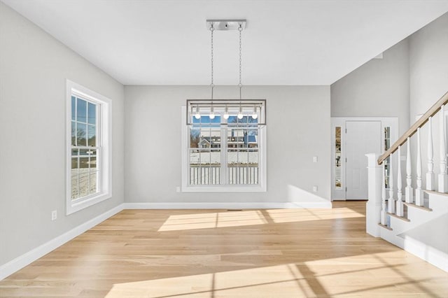 unfurnished dining area with wood finished floors, a notable chandelier, baseboards, and stairs