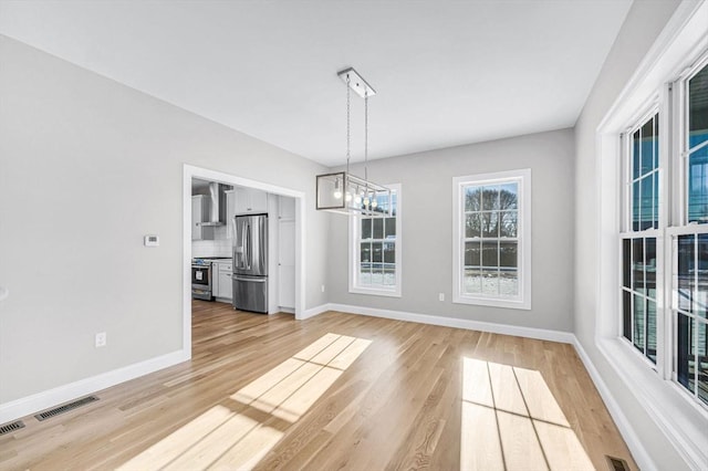 unfurnished dining area featuring baseboards, visible vents, light wood finished floors, and an inviting chandelier