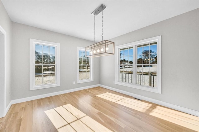 unfurnished dining area featuring baseboards, visible vents, and wood finished floors