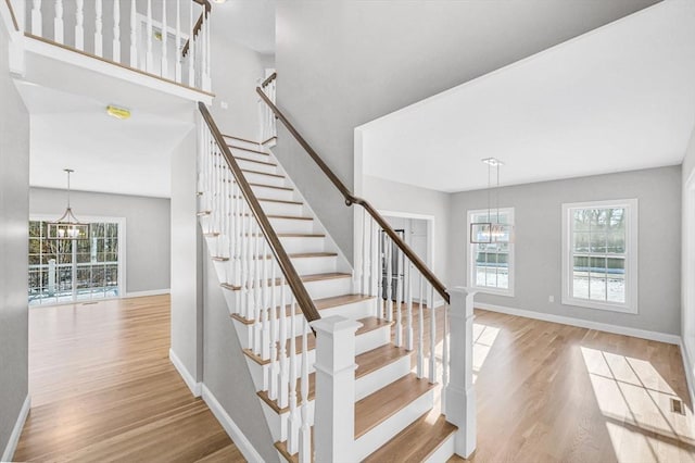 staircase with wood finished floors, baseboards, and an inviting chandelier