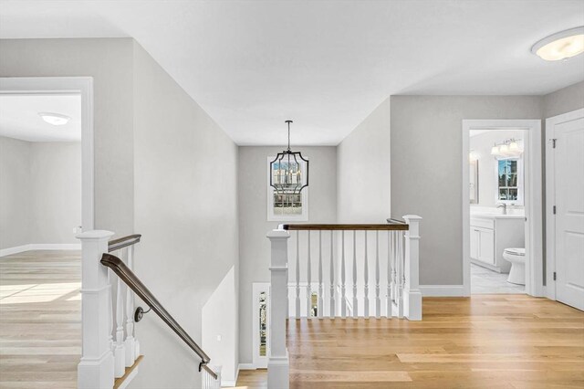 hallway with baseboards, a sink, light wood-style flooring, and an upstairs landing