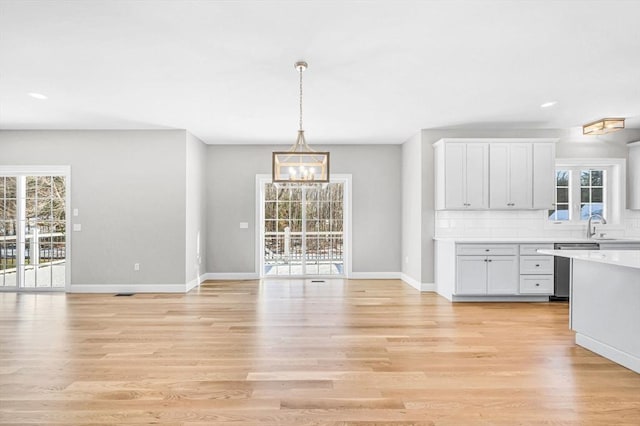 unfurnished dining area with light wood-style floors, a chandelier, a sink, and baseboards