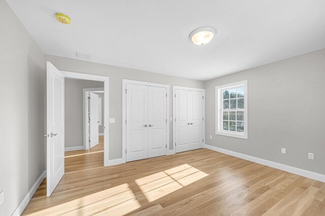 unfurnished bedroom with baseboards, light wood-style floors, and multiple closets