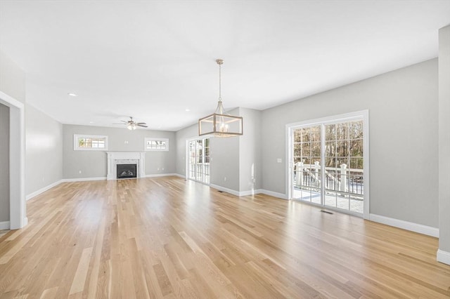 unfurnished living room with light wood-style floors, a fireplace, baseboards, and ceiling fan with notable chandelier