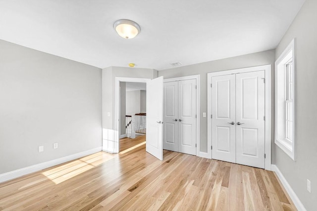 unfurnished bedroom featuring visible vents, light wood-style flooring, baseboards, and two closets