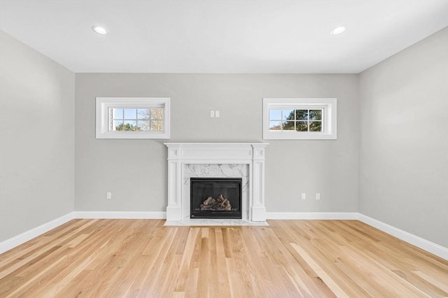 unfurnished living room featuring a healthy amount of sunlight, light wood finished floors, and a premium fireplace