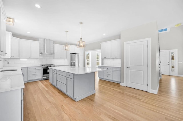 kitchen with light wood-style flooring, a sink, light countertops, appliances with stainless steel finishes, and wall chimney exhaust hood