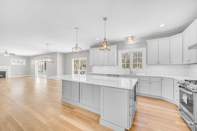 kitchen featuring light wood-style flooring, a kitchen island, open floor plan, backsplash, and stainless steel range with gas stovetop