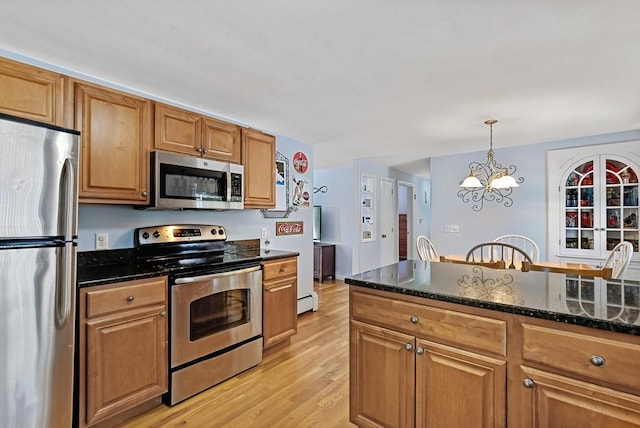 kitchen featuring pendant lighting, appliances with stainless steel finishes, an inviting chandelier, light hardwood / wood-style floors, and dark stone countertops