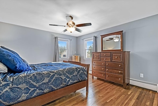 bedroom with ceiling fan, wood-type flooring, and a baseboard heating unit