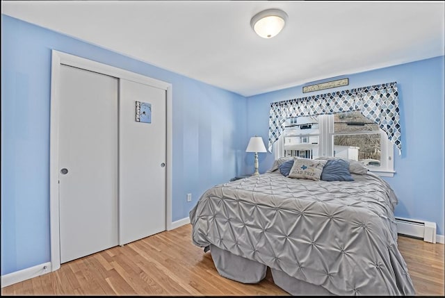 bedroom with a closet, a baseboard heating unit, and light hardwood / wood-style floors