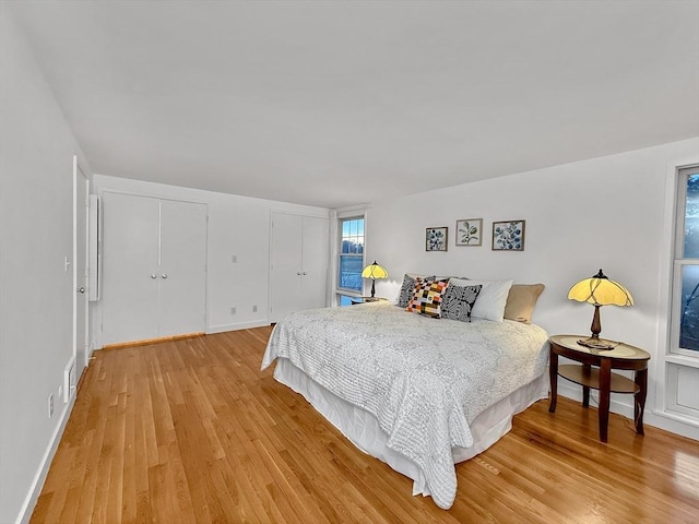 bedroom featuring light wood-style flooring, baseboards, and multiple closets