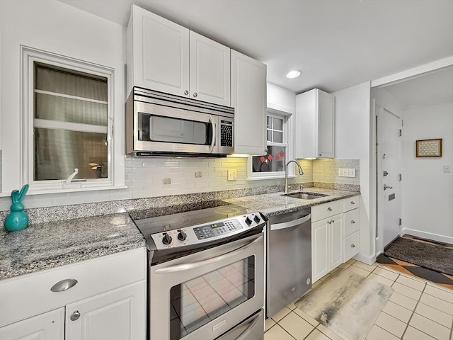 kitchen featuring stainless steel appliances, decorative backsplash, white cabinets, a sink, and light tile patterned flooring