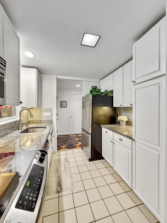 kitchen featuring backsplash, electric range, freestanding refrigerator, white cabinets, and a sink