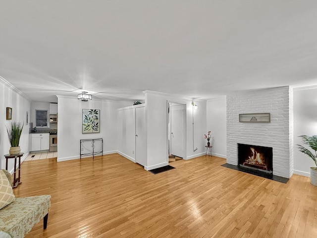 living room with light wood-style flooring, a fireplace, ornamental molding, and baseboards