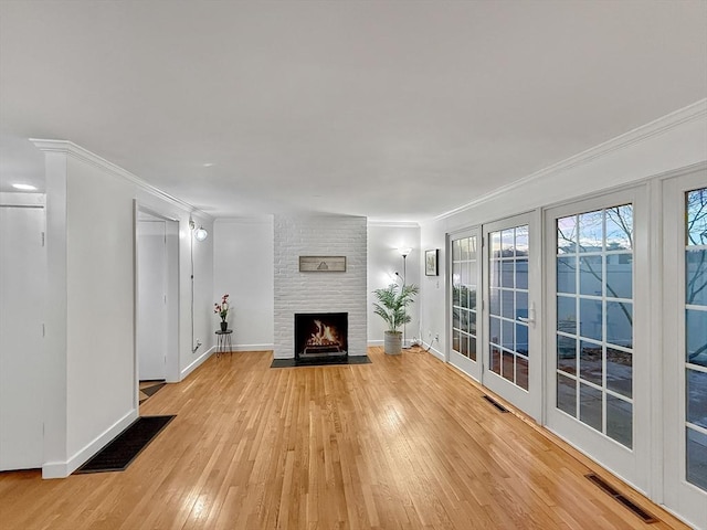 unfurnished living room with light wood finished floors, a brick fireplace, visible vents, and ornamental molding