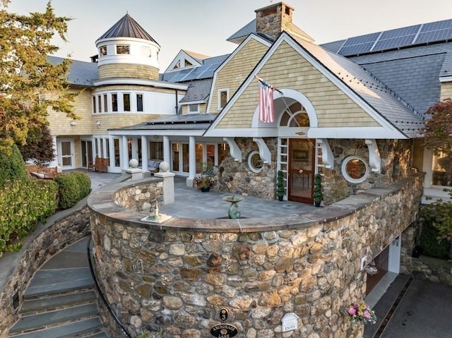 3 Anchorage Ln, Marblehead, MA 01945 - rear view of house with roof mounted solar panels, a chimney, stone siding, a standing seam roof, and a patio area