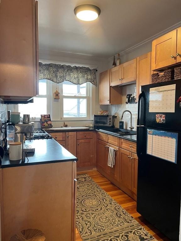 kitchen with decorative backsplash, ornamental molding, freestanding refrigerator, a sink, and light wood-type flooring