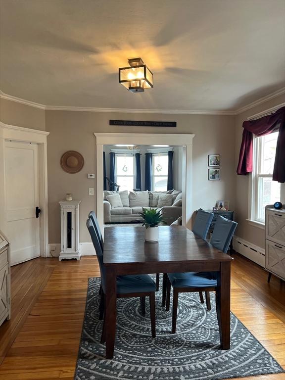 dining space featuring baseboards, ornamental molding, a baseboard radiator, and light wood-style floors