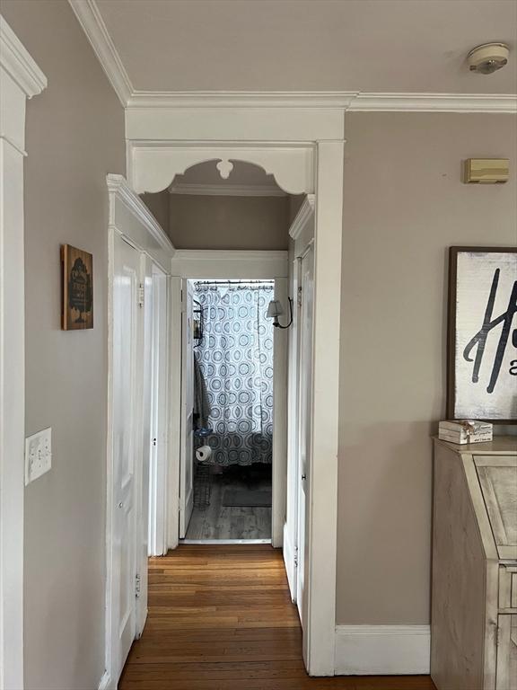 corridor featuring baseboards, wood finished floors, and crown molding