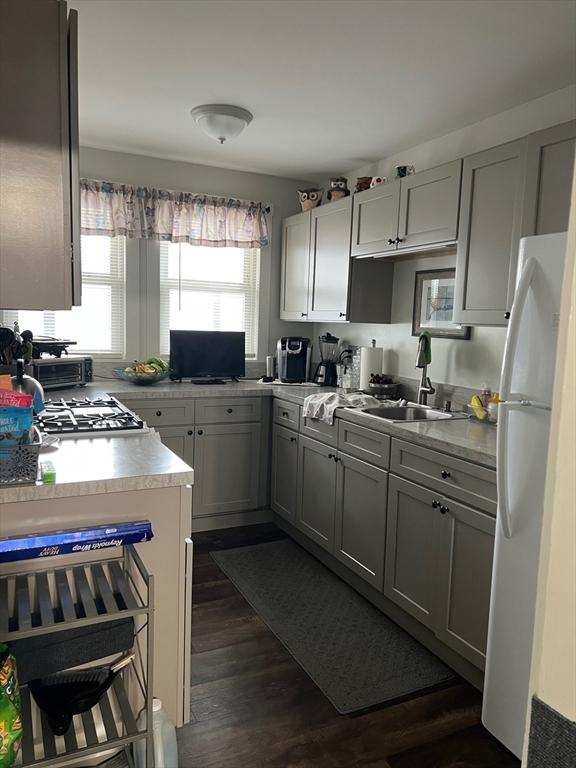 kitchen featuring dark wood-type flooring, freestanding refrigerator, light countertops, gray cabinetry, and a sink