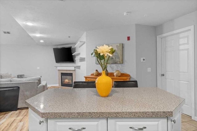 216 Reservoir St Unit 304, Holden, MA 01520 - kitchen with open floor plan, white cabinetry, a center island, visible vents, and a glass covered fireplace