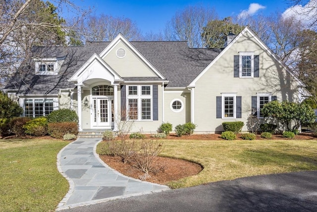 new england style home with roof with shingles, a chimney, and a front yard