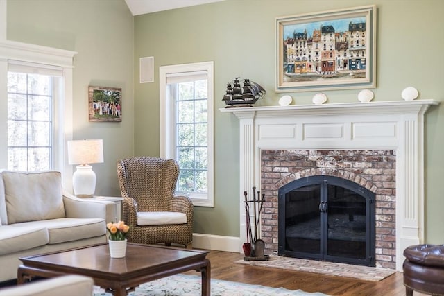 living room featuring baseboards, a brick fireplace, and wood finished floors