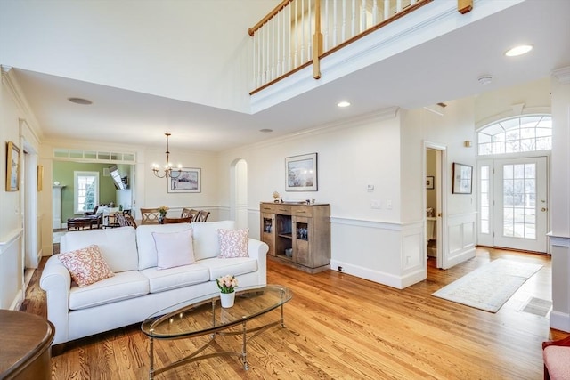 living room featuring a notable chandelier, light wood-style floors, wainscoting, crown molding, and a towering ceiling