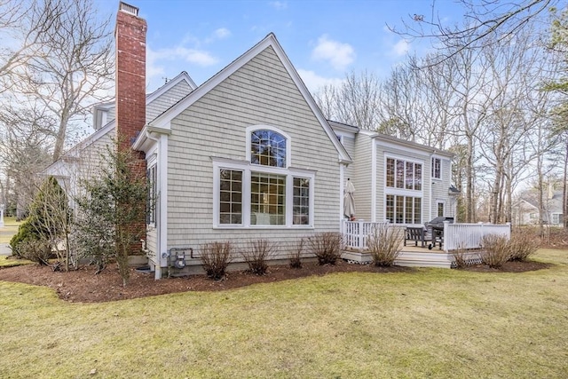 rear view of property featuring a wooden deck, a lawn, and a chimney