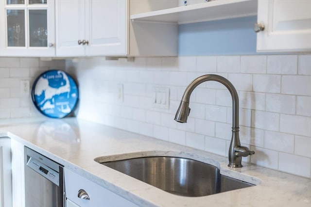 kitchen with tasteful backsplash, white cabinets, dishwasher, and a sink