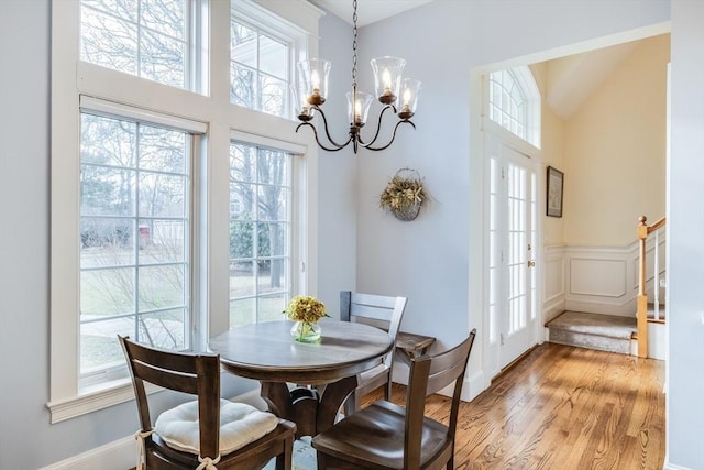 dining area featuring light wood-type flooring, a wainscoted wall, stairway, an inviting chandelier, and a towering ceiling