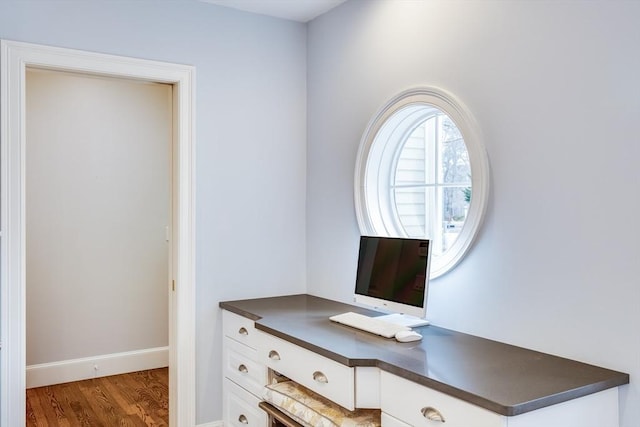 office space with wood finished floors, built in desk, and baseboards