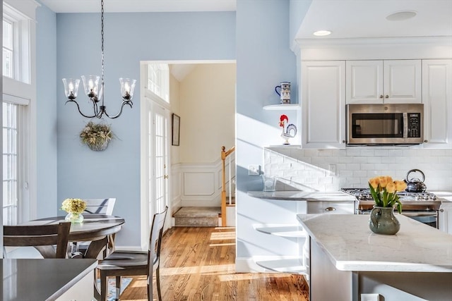 kitchen featuring light wood-type flooring, backsplash, stainless steel appliances, white cabinets, and a chandelier