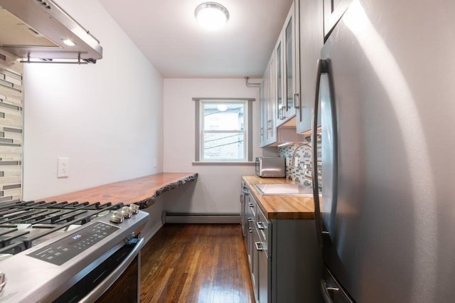 kitchen featuring baseboard heating, appliances with stainless steel finishes, tasteful backsplash, and wooden counters