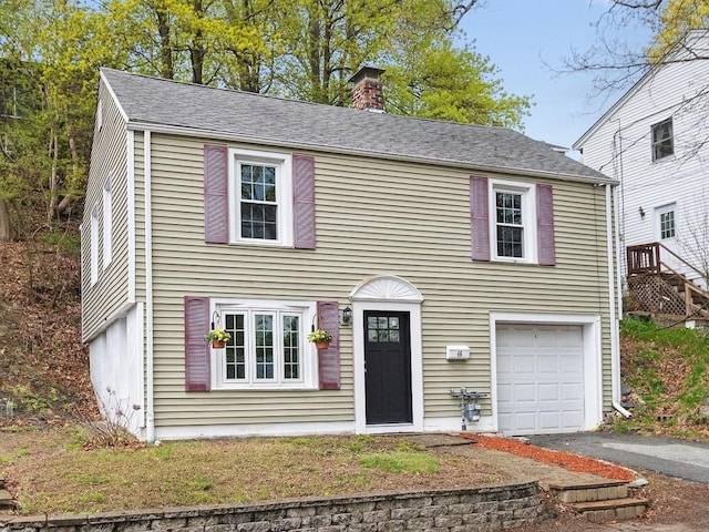 colonial house featuring a garage, a chimney, and driveway