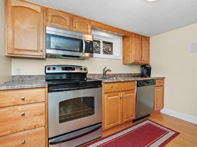 kitchen featuring baseboards, appliances with stainless steel finishes, a sink, and light wood-style flooring