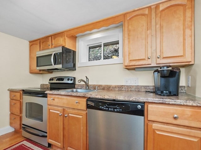 kitchen featuring light wood-style floors, a sink, appliances with stainless steel finishes, and light countertops