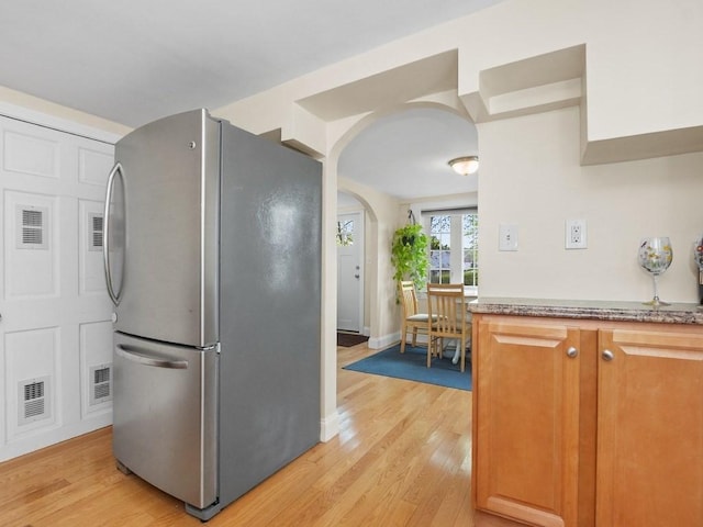 kitchen featuring visible vents, freestanding refrigerator, light wood finished floors, and arched walkways